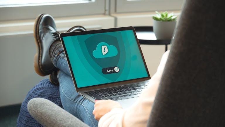 A person wearing boots relaxes with a laptop displaying a VPN save screen indoors.